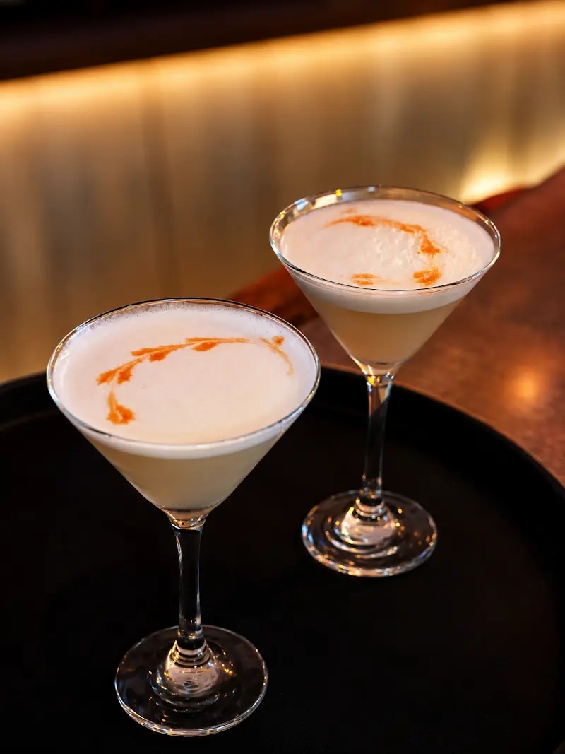 Dos cócteles espumosos en copas de martini sobre una bandeja negra
