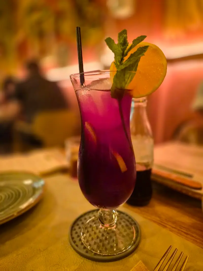 Cóctel morado con naranja, hierbabuena y pajita en una mesa del restaurante