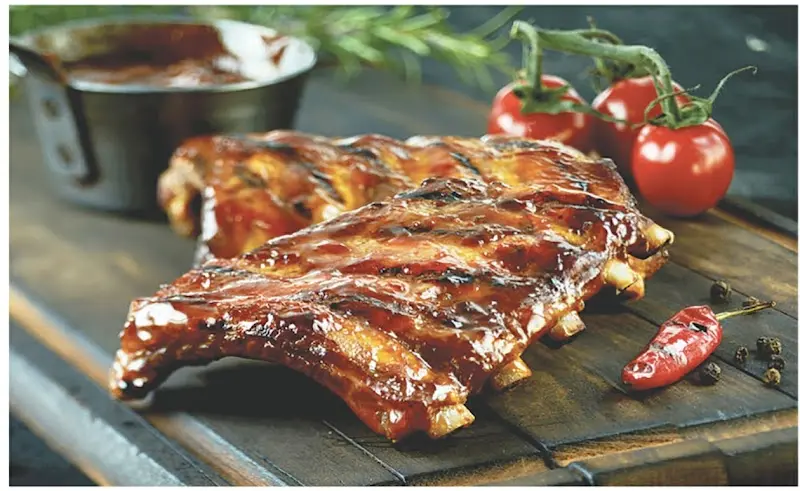 Costillas de cerdo a la barbacoa glaseadas sobre una tabla con tomates y guindilla