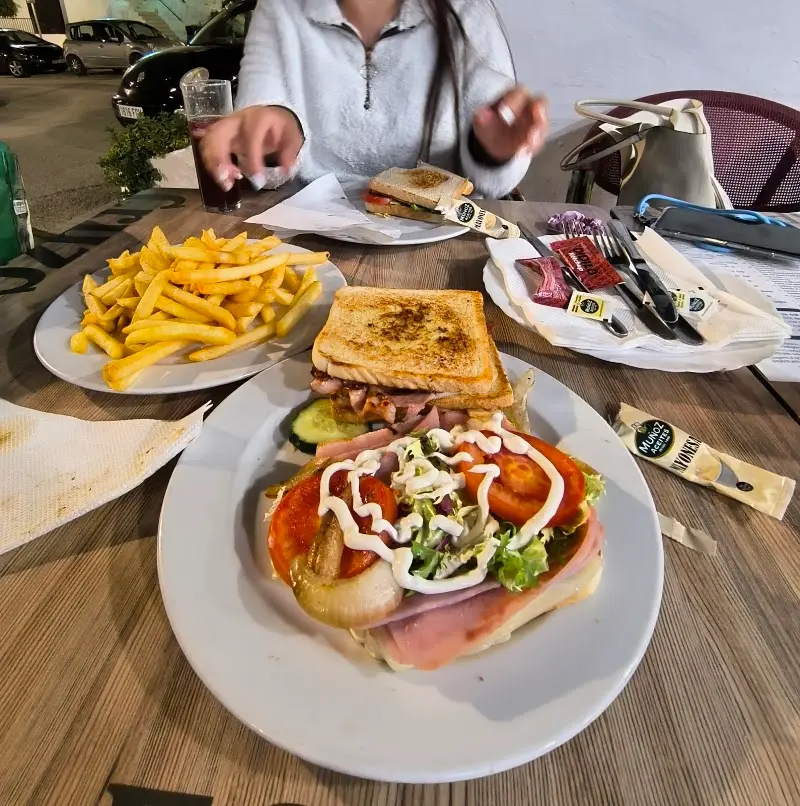 Sándwich mixto con beicon, tomate, cebolla y mayonesa, con patatas fritas en la terraza