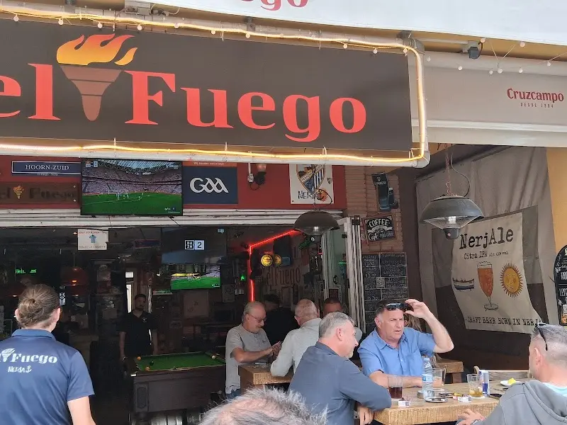 Clientes en la entrada del bar bajo el rótulo El Fuego, con fútbol en las pantallas