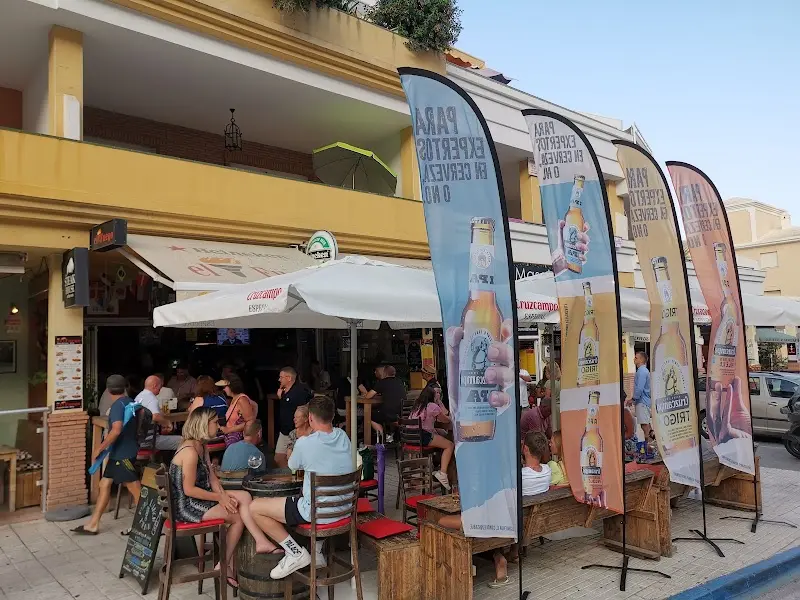 Terraza animada al atardecer con banderas de cerveza, sombrillas y mesas de barril