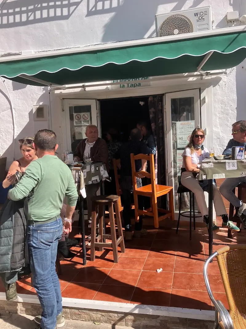 Clientes en la terraza y la entrada del bar, bajo un toldo verde en un día soleado