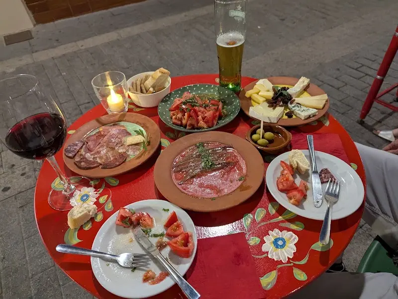 Mesa roja con tabla de quesos, embutidos, anchoas, tomate aliñado, cerveza y vino tinto