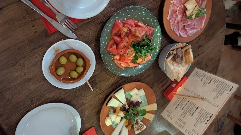Vista cenital de tapas: aceitunas, ensalada de tomate, jamón, quesos y la carta