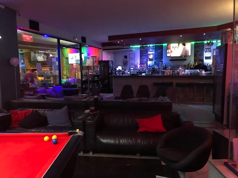 Salón con mesa de billar, sofás de piel, barra iluminada y pantallas de televisión