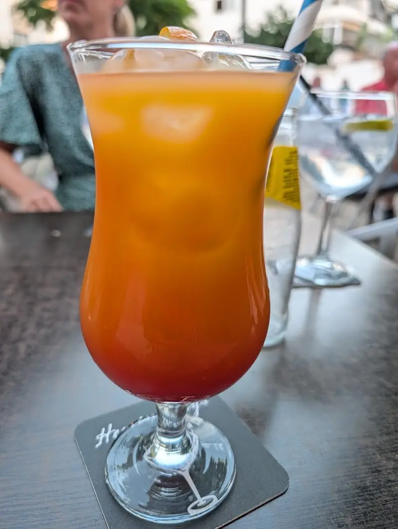 Cóctel naranja con degradado rojo y hielo en copa alta, en la terraza