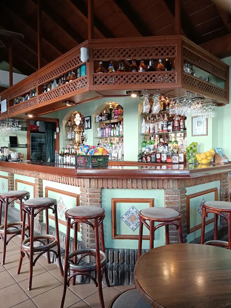 Barra de madera y azulejos con taburetes y estanterías de botellas en arcos en Hemingway's