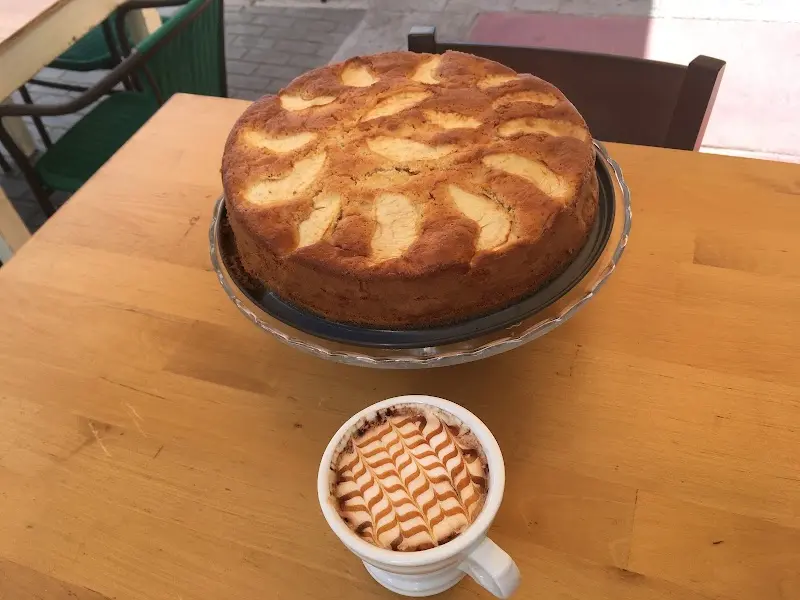 Bizcocho casero de manzana sobre una fuente junto a un café con dibujo de caramelo