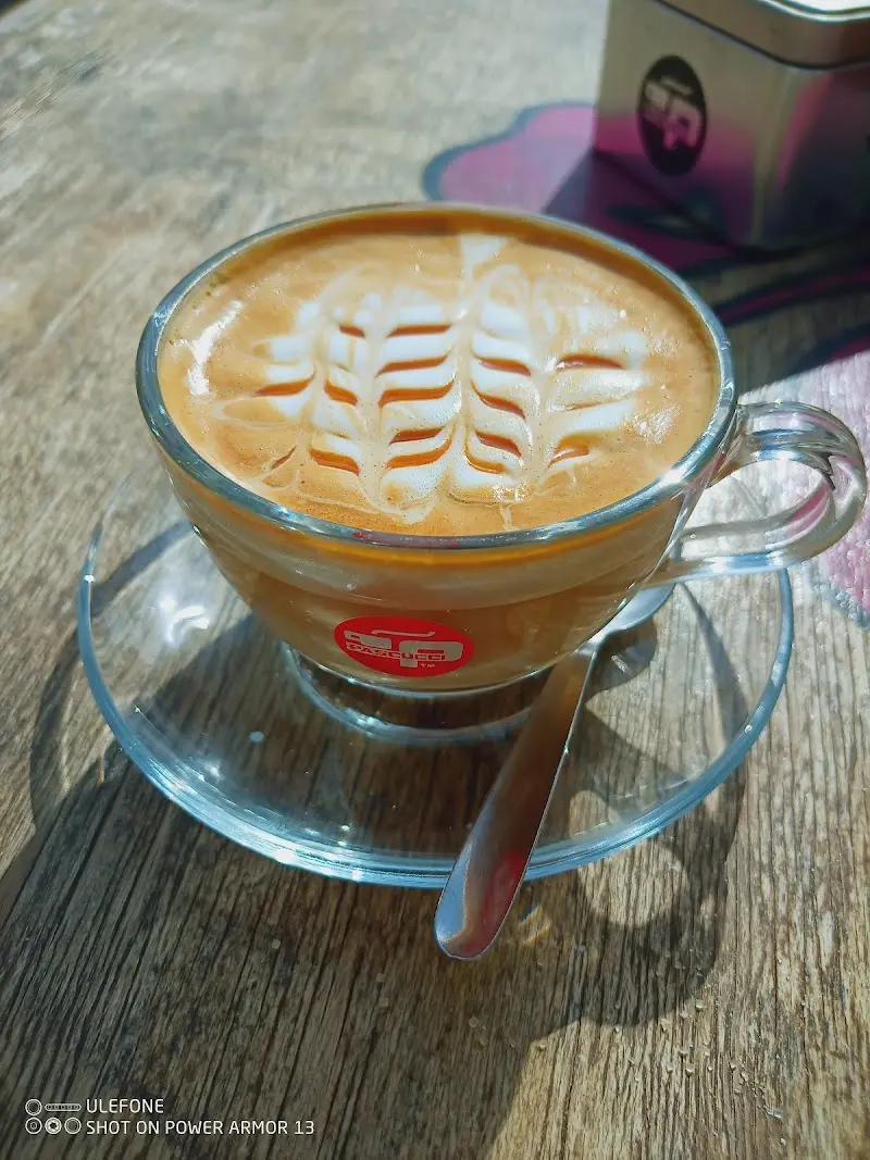 Capuchino con arte latte en forma de hoja en taza de cristal sobre mesa de madera