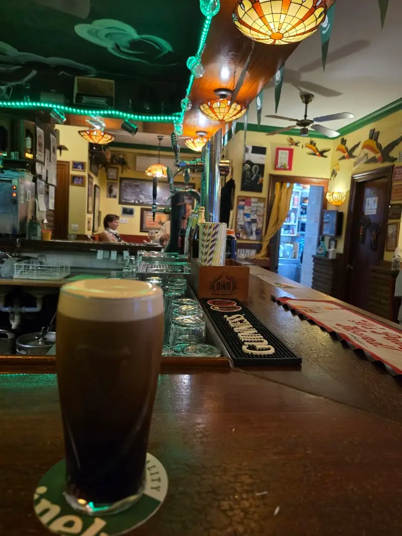 Pinta de cerveza negra en la barra, con lámparas de colores y paredes decoradas al fondo