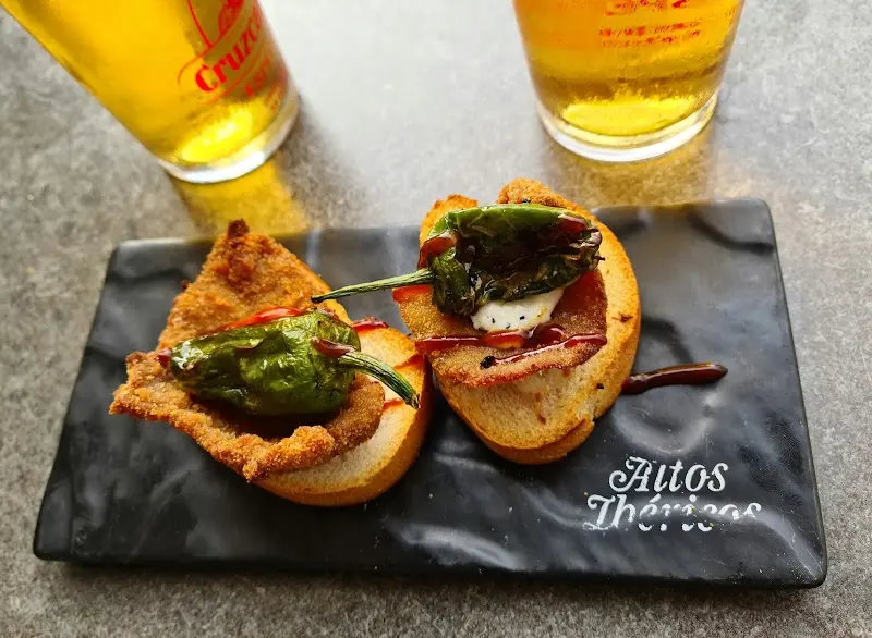 Dos montaditos con carne empanada y pimiento frito sobre pizarra, con cañas de cerveza