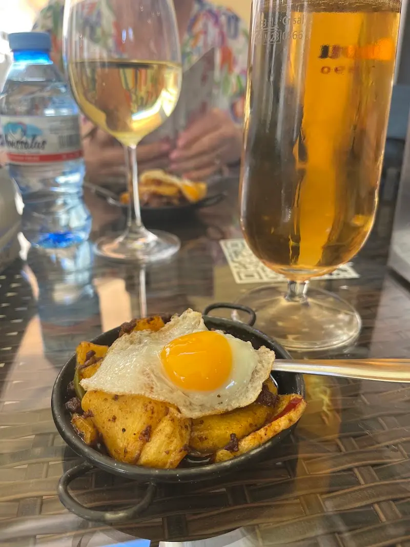 Cazuelita de patatas con huevo de codorniz frito junto a una copa de vino y una cerveza