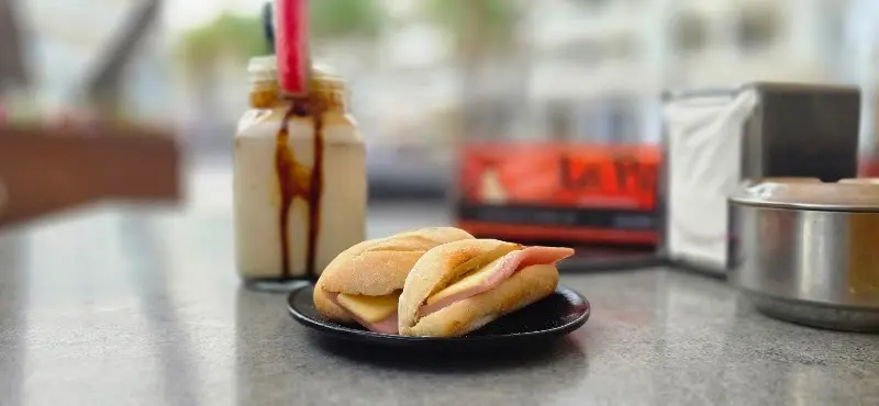 Bocadillo pequeño de jamón york y queso con un batido en tarro de cristal