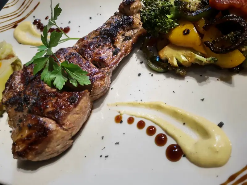 Carne a la parrilla con verduras asadas y salsa de mostaza decorando el plato