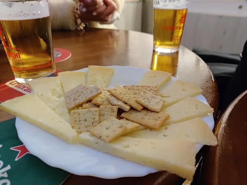 Plato de queso en cuñas con galletas saladas y dos cañas de cerveza
