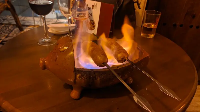 Chorizos flambeados en un asador de barro con forma de cerdito sobre la mesa