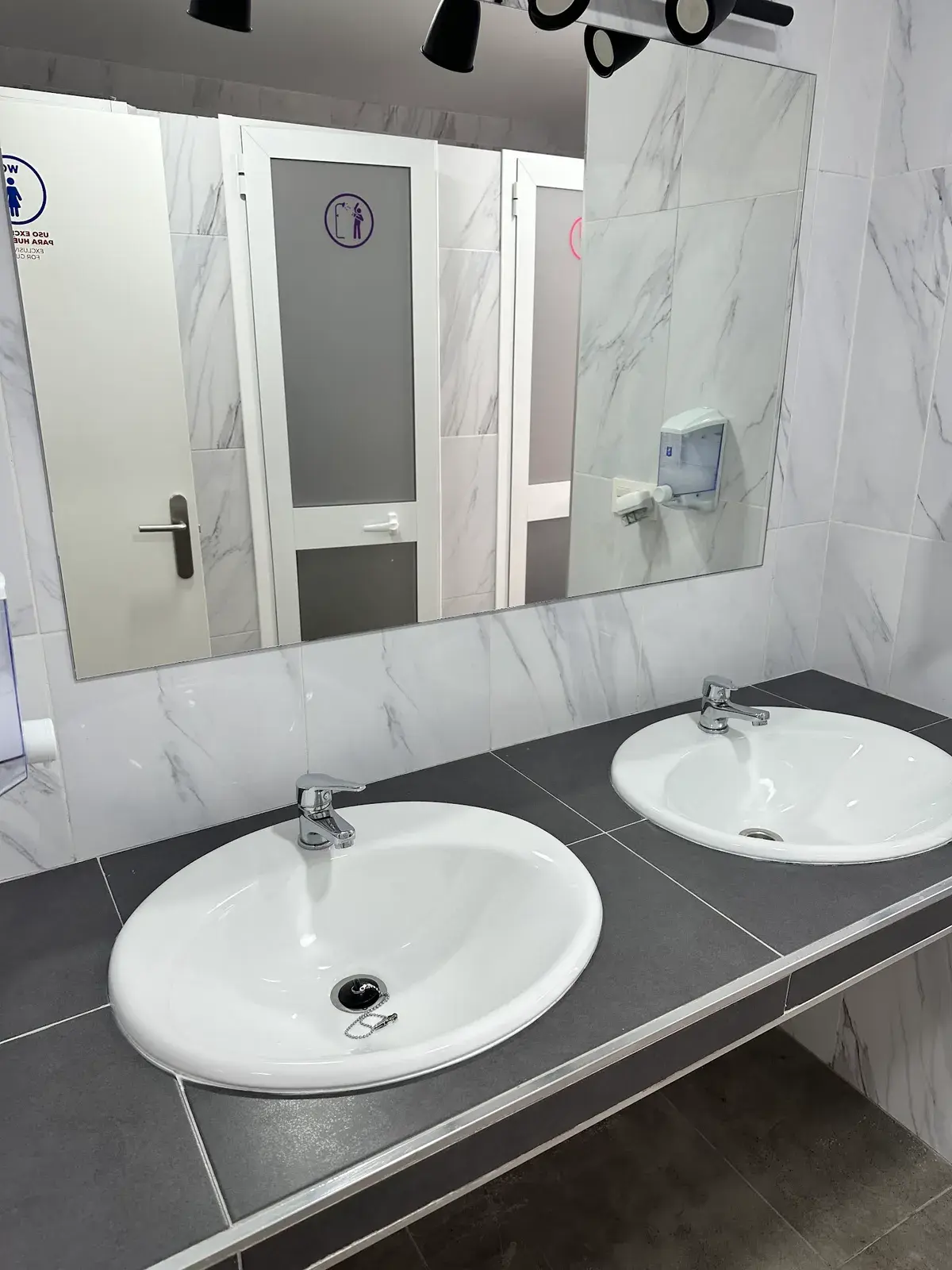 Baño compartido con dos lavabos y paredes de azulejo blanco