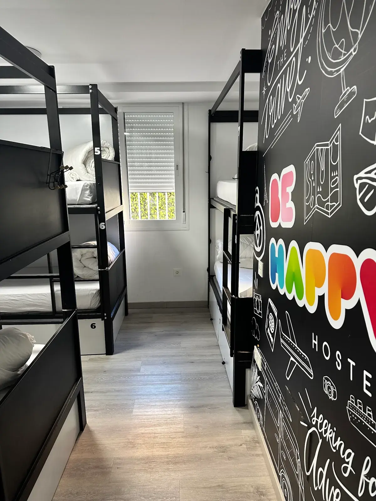 Dormitorio con literas y una pared pintada con el logotipo de Be Happy