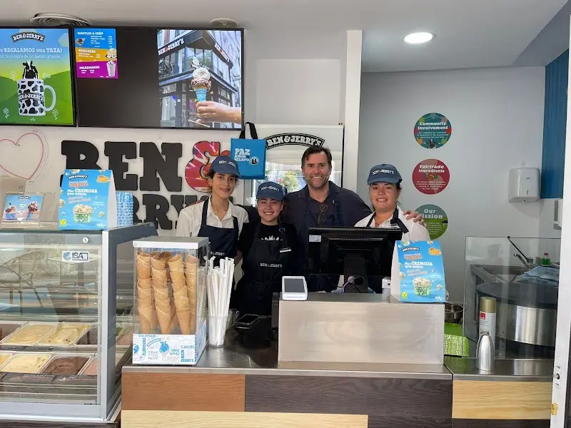 Equipo de la heladería sonriendo tras el mostrador con conos de barquillo y vitrina de helados