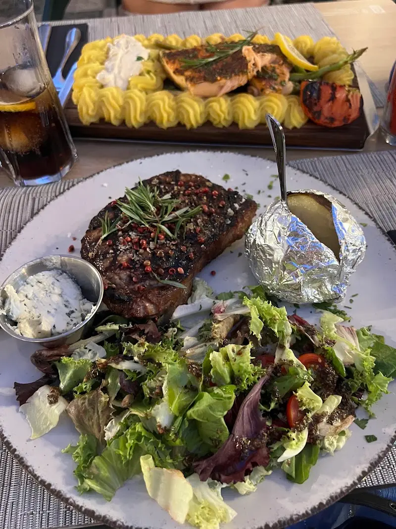Entrecot con pimienta rosa, ensalada y patata asada; detrás, salmón con puré de patata