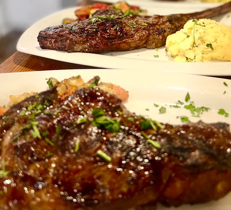 Dos chuletones a la brasa con perejil y puré de patata, servidos en plato blanco