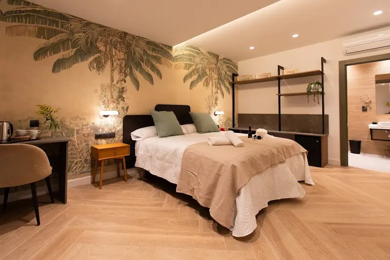Habitación con mural de palmeras, cama de matrimonio, estantes metálicos y baño al fondo