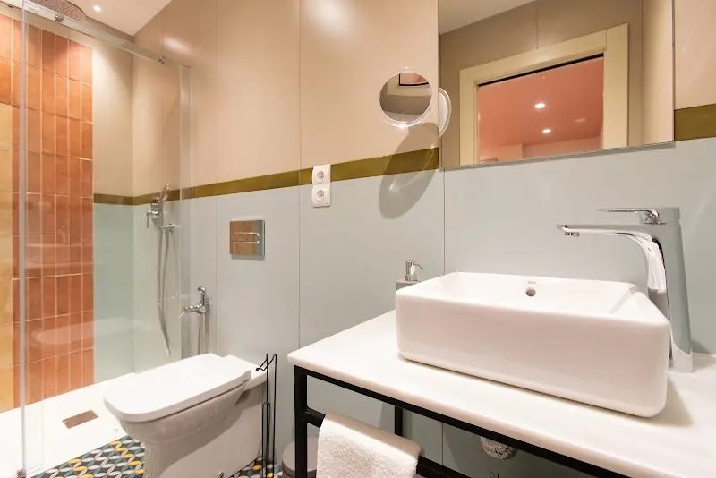 Baño con ducha de azulejos terracota, lavabo sobre encimera blanca y espejo de aumento
