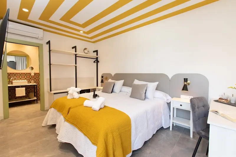 Habitación con techo de rayas amarillas, cama grande con manta mostaza y baño abierto