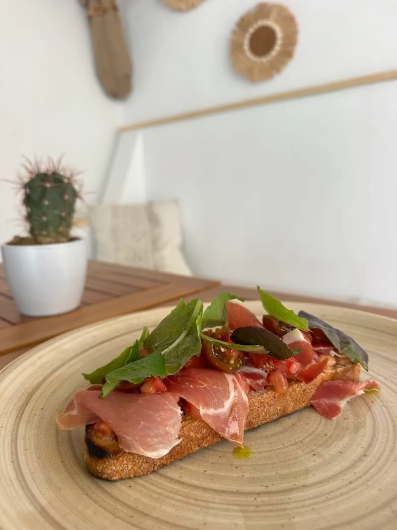 Tostada de jamón con tomate y hojas de albahaca en Brisa Brunch, con un cactus al fondo