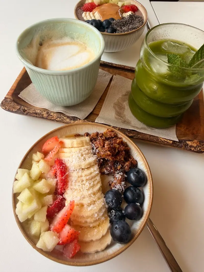 Bol de fruta con plátano, fresas, arándanos y granola, con café con leche y zumo verde