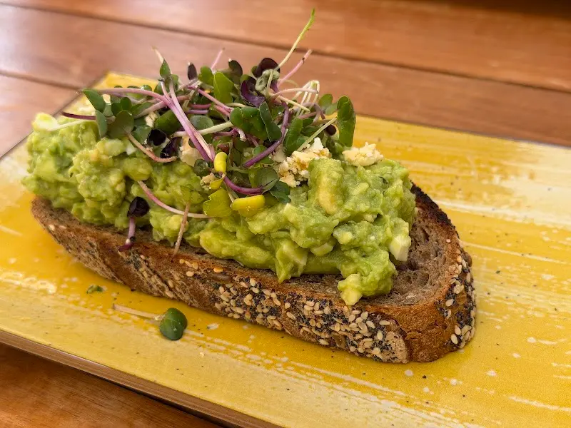 Tostada de pan de masa madre con aguacate, huevo picado y brotes sobre un plato amarillo