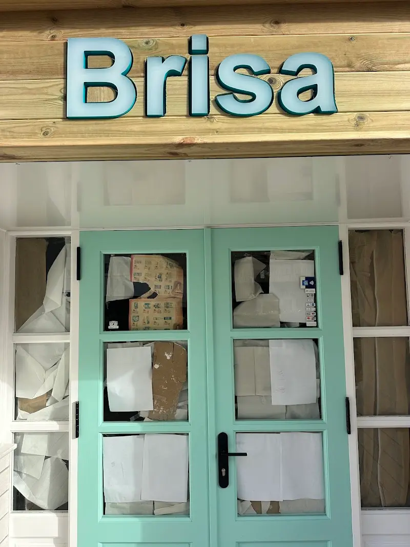 Letrero de Brisa sobre madera y puertas verde agua con los cristales tapados con papeles