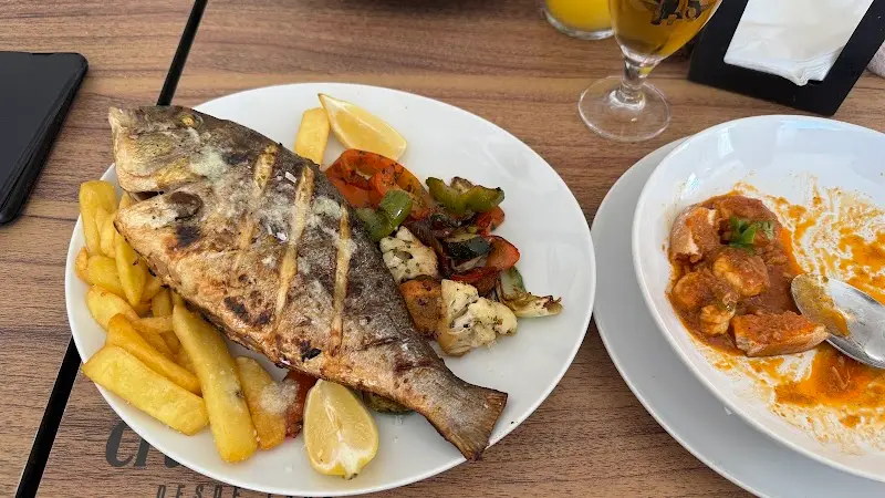 Dorada a la plancha con patatas fritas y verduras asadas, junto a un plato de guiso