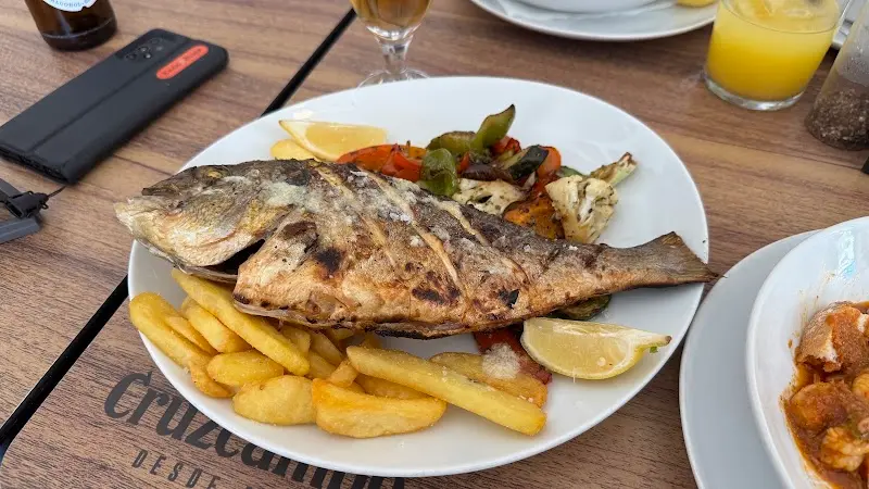 Plato de dorada a la brasa con limón, patatas fritas y verduras a la parrilla en la mesa