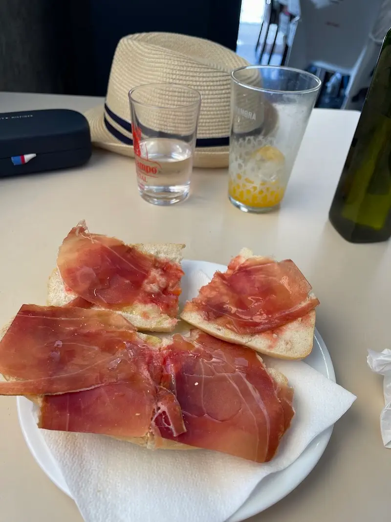 Tostada con tomate y jamón serrano en un plato, con vasos de agua y zumo
