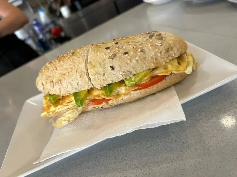Bocadillo de pan de semillas con tortilla, tomate y aguacate servido en la barra