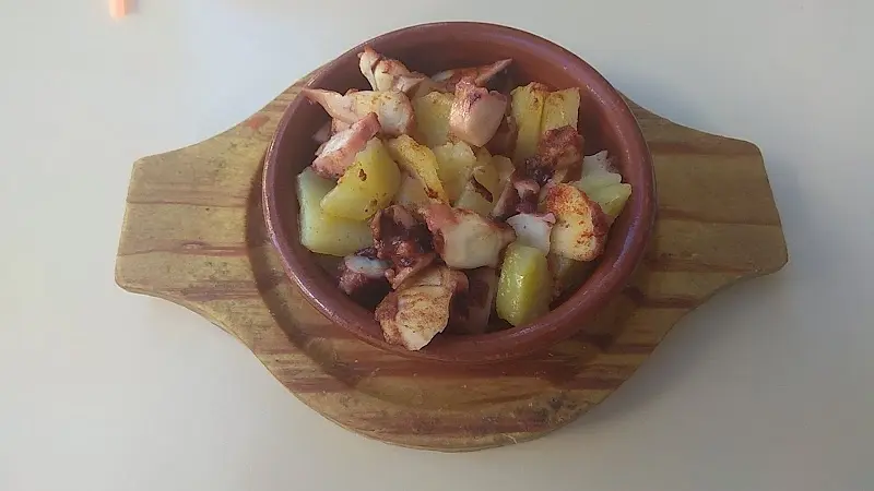 Cazuela de barro con pulpo y patatas con pimentón sobre una tabla de madera