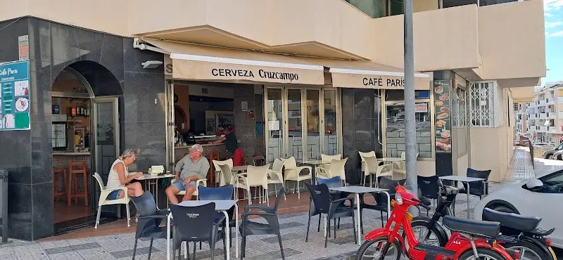 Terraza de Cafe Paris con sillas blancas y negras bajo el toldo de Cerveza Cruzcampo