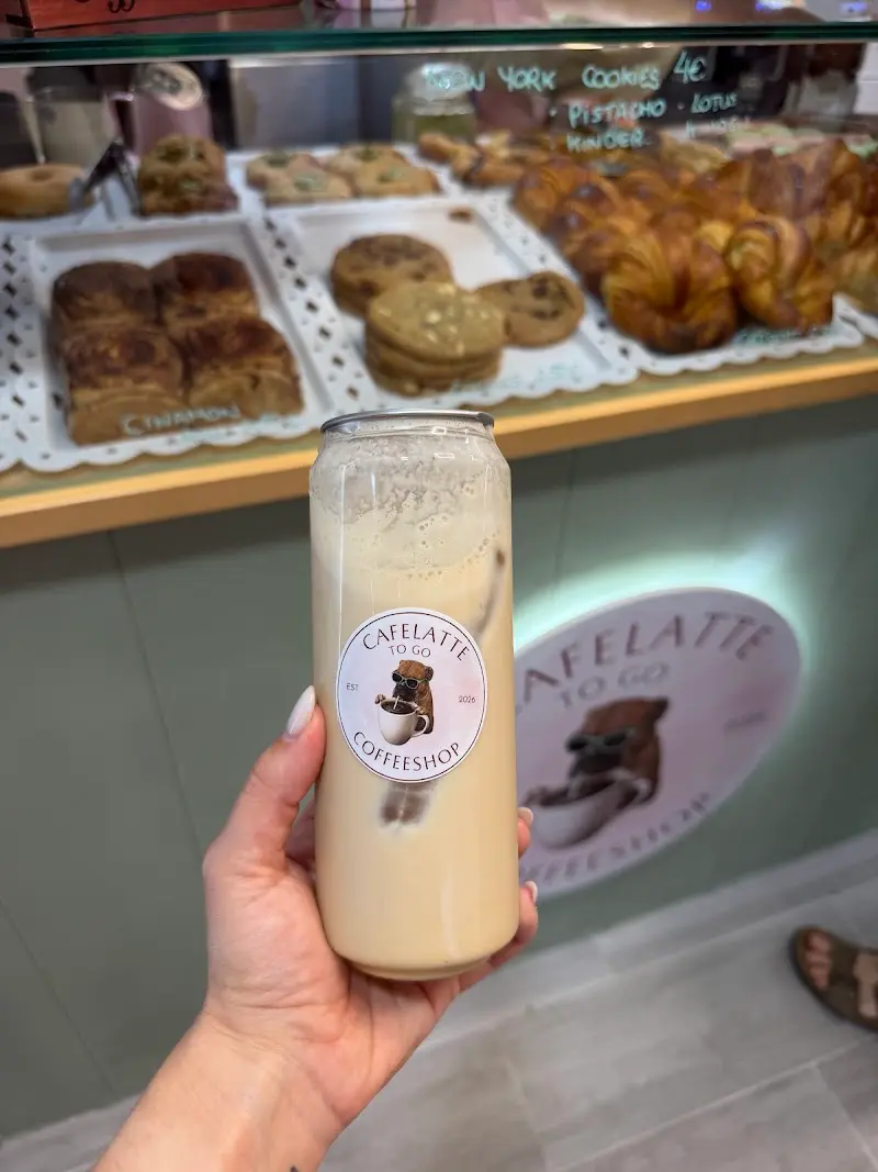 Café con leche frío en lata de cristal con el logo, delante de la vitrina de galletas y cruasanes