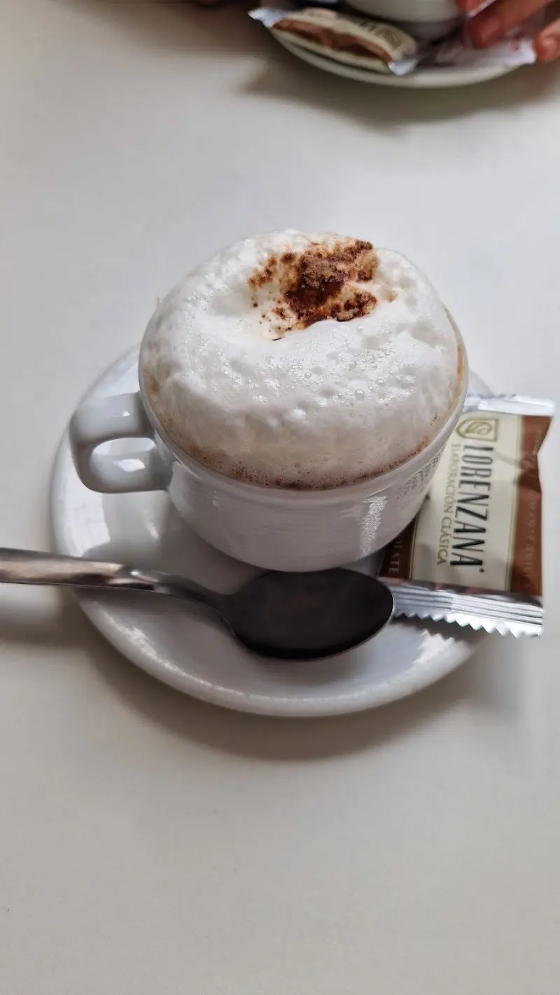 Capuchino con espuma de leche y canela, con una galleta en el plato
