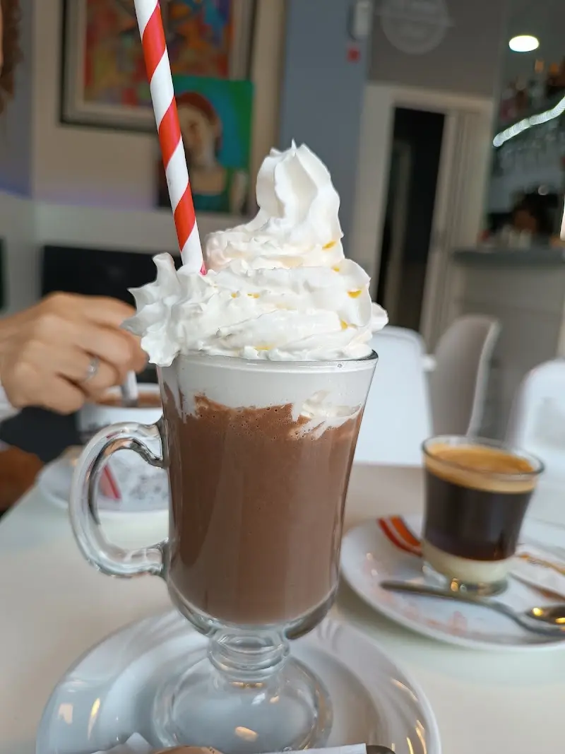 Batido de chocolate con nata montada y pajita de rayas, junto a un café cortado