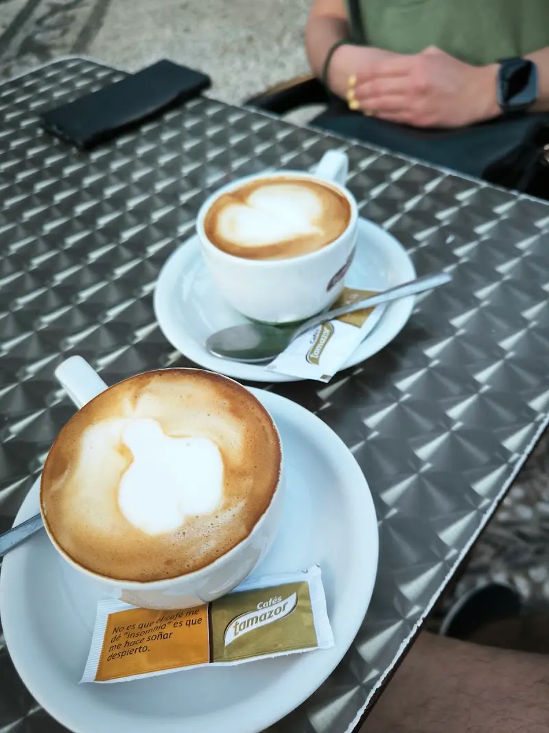 Dos cafés con leche con espuma en forma de corazón sobre una mesa metálica