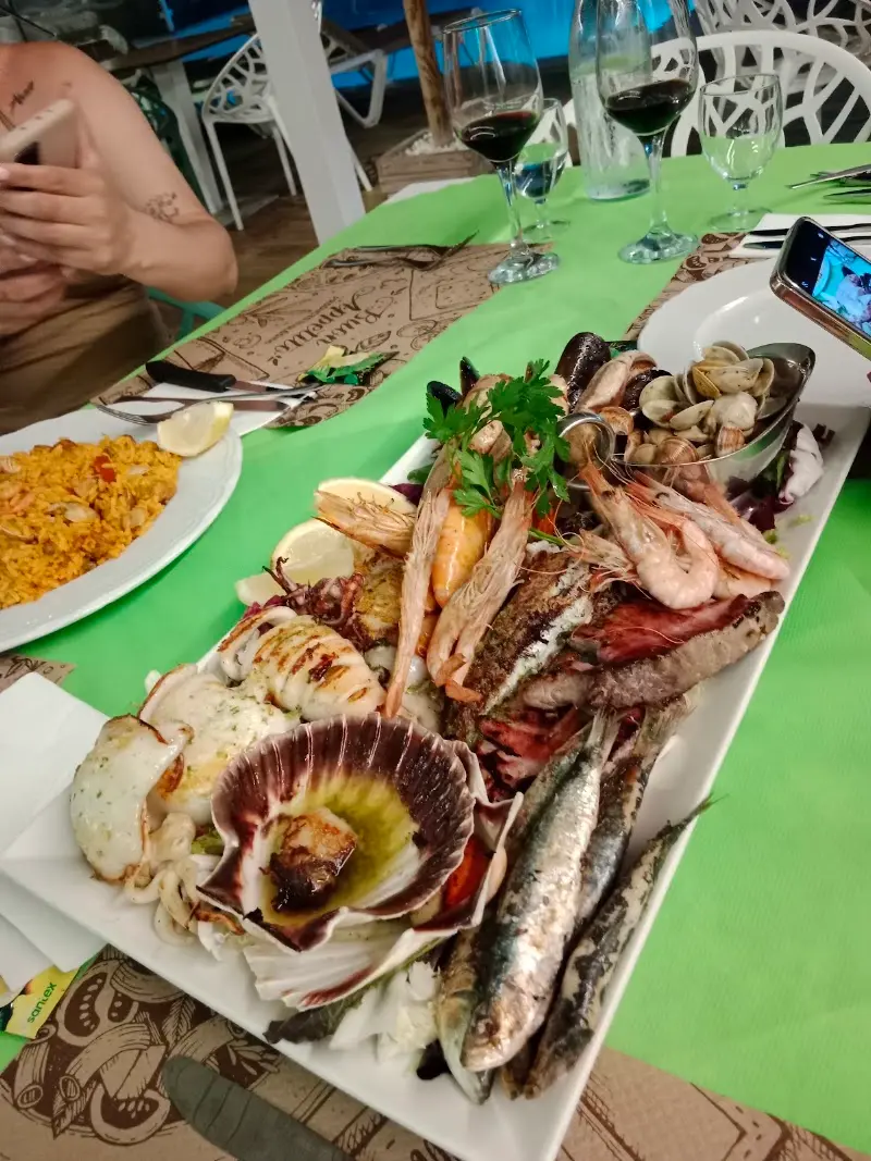 Parrillada de marisco y pescado con zamburiñas, gambas, sardinas y almejas, junto a un plato de paella