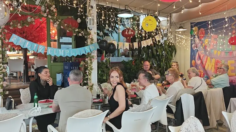 Terraza llena de clientes con guirnaldas, globos y luces de colores por una celebración