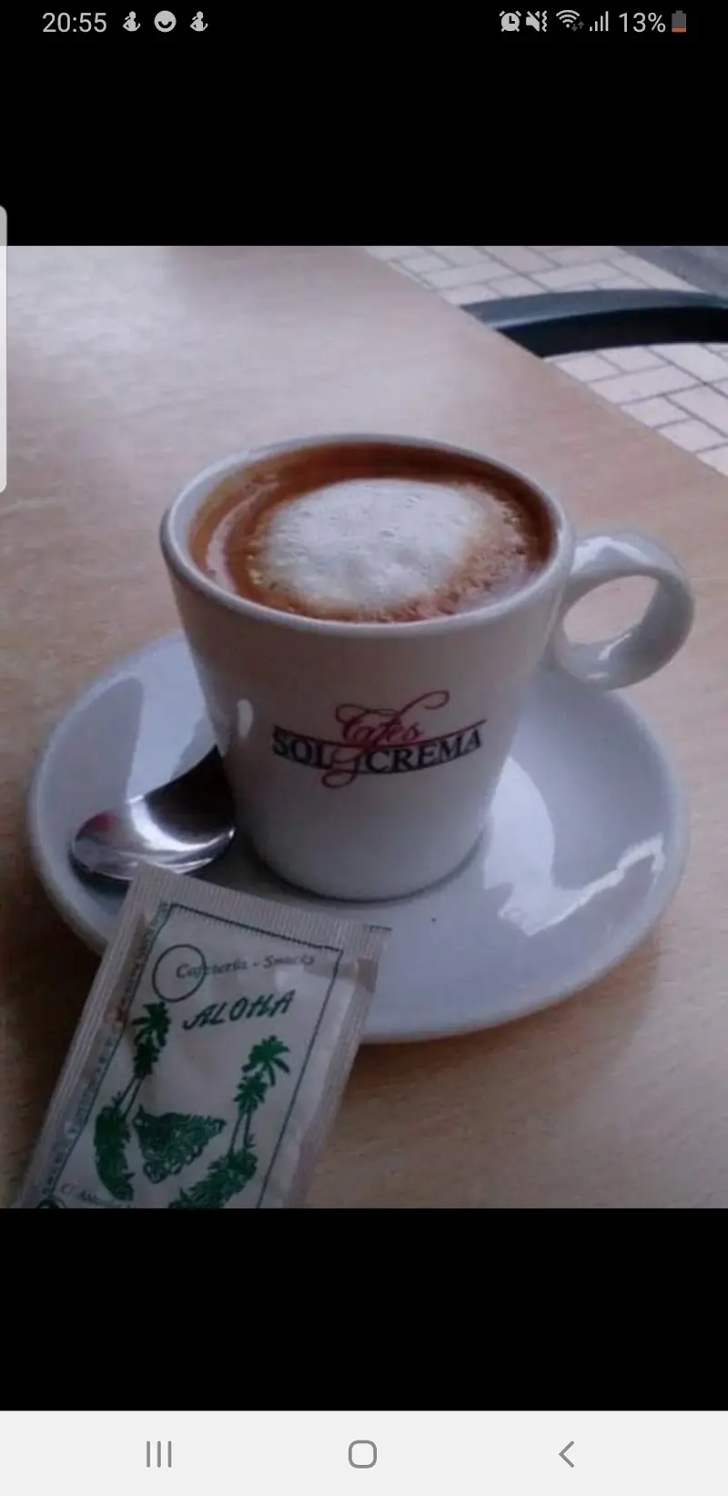 Café con leche en taza blanca con un sobre de azúcar de la Cafetería Aloha