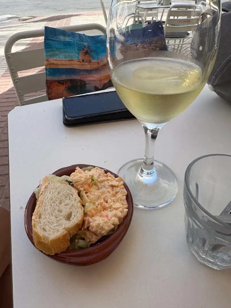 Copa de vino blanco y cuenco de ensaladilla con pan en una mesa de la terraza
