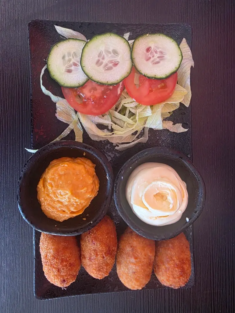 Croquetas con dos salsas para mojar, tomate, pepino y lechuga vistas desde arriba
