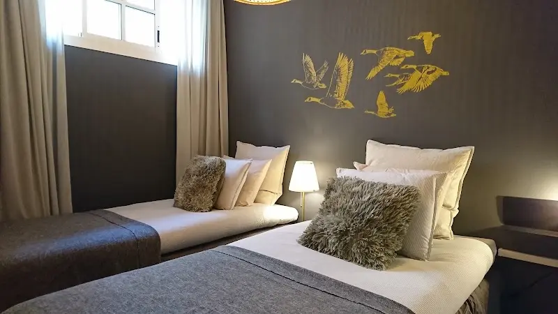 Habitación con dos camas individuales, cojines de pelo y aves doradas pintadas en la pared
