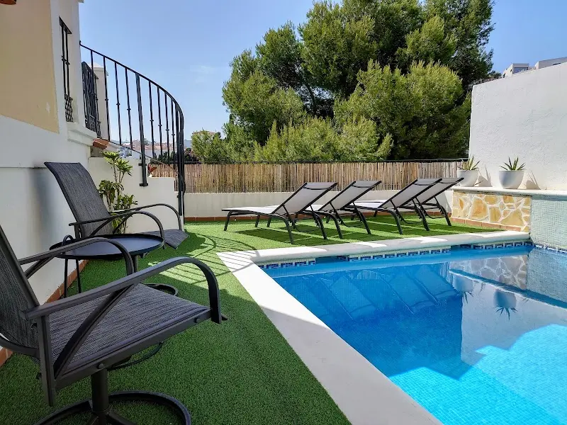 Piscina de Carmen Rooms con césped artificial, tumbonas y sillas junto a la escalera